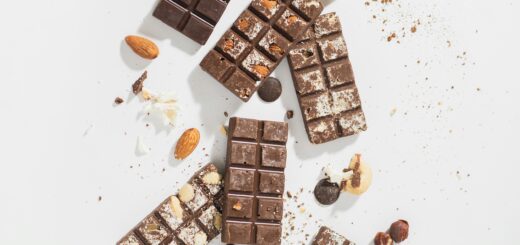 An artistic arrangement of dark, milk, and white chocolate bars with almonds on a white surface.