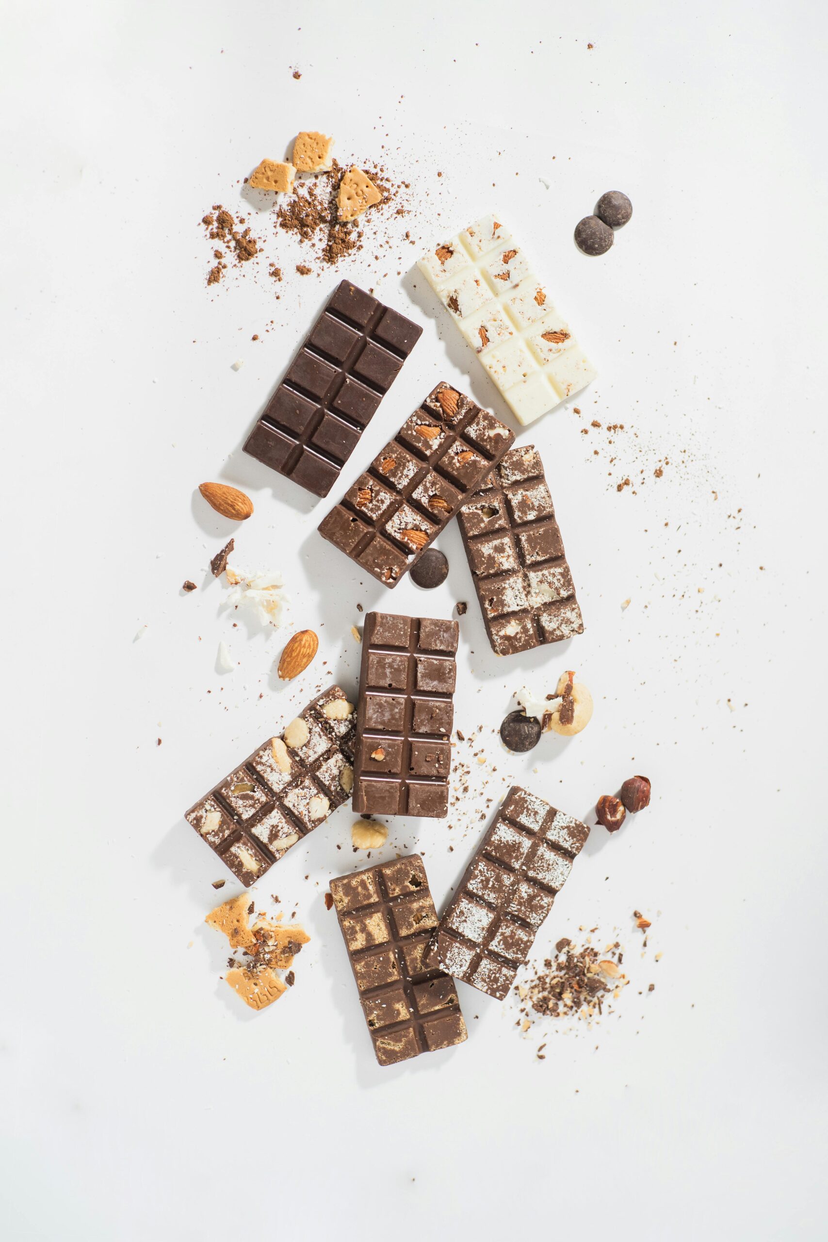 An artistic arrangement of dark, milk, and white chocolate bars with almonds on a white surface.